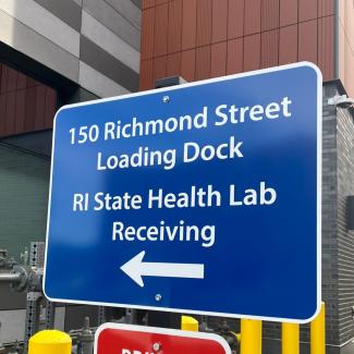 Sign that reads "150 Richmond Street Loading Dock, RI STate Health Lab Receiving". An arrow points towards the parking lot entrance.
